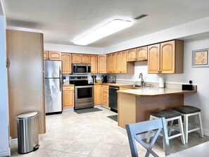 A modern kitchen with wooden cabinets, stainless steel appliances, and a bar area with stools. - The Lakeplace on Flathead close to GNP (Polson)