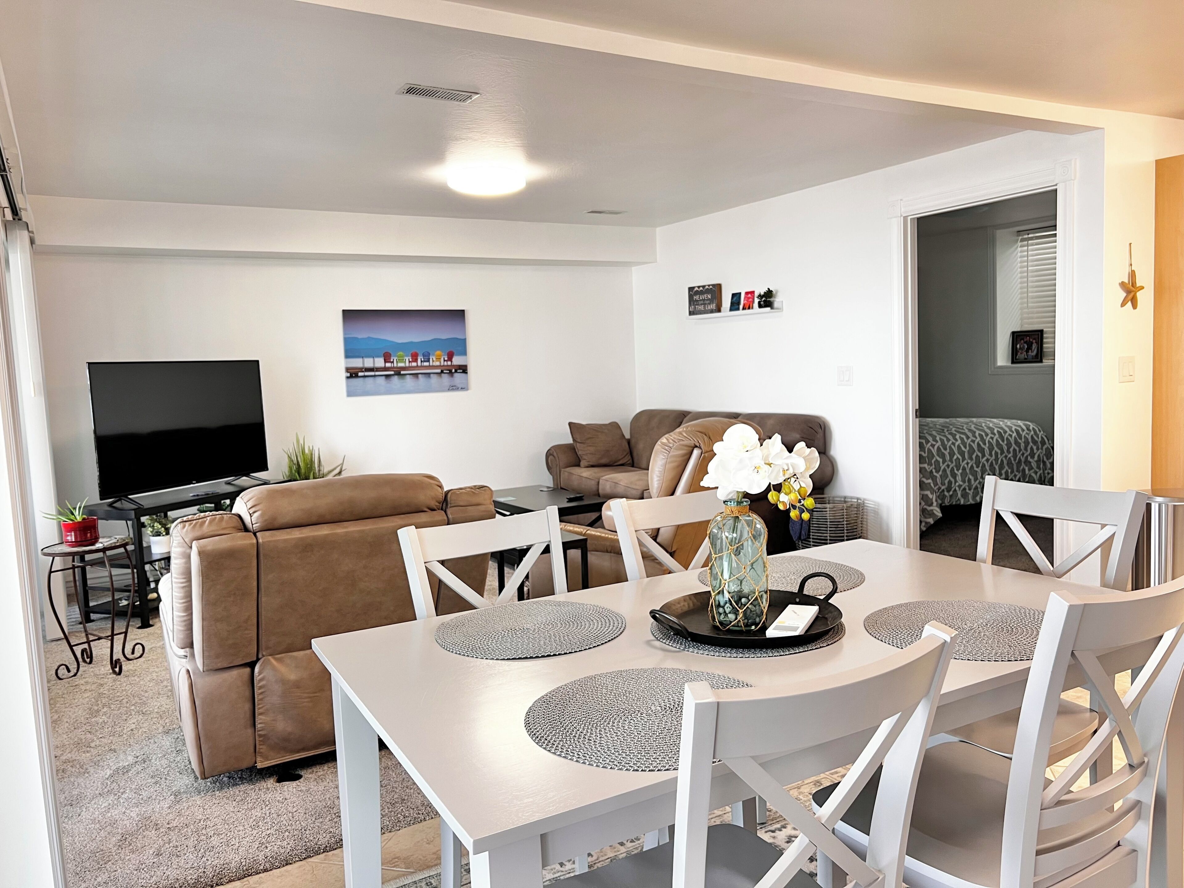 A modern living room with a flat-screen TV, a sofa, a dining table with chairs, and a decorative vase with flowers.