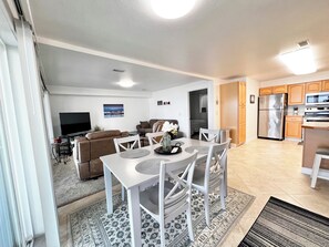 A modern living room with a sofa, TV, and dining area with chairs and a table. - The Lakeplace on Flathead close to GNP (Polson)