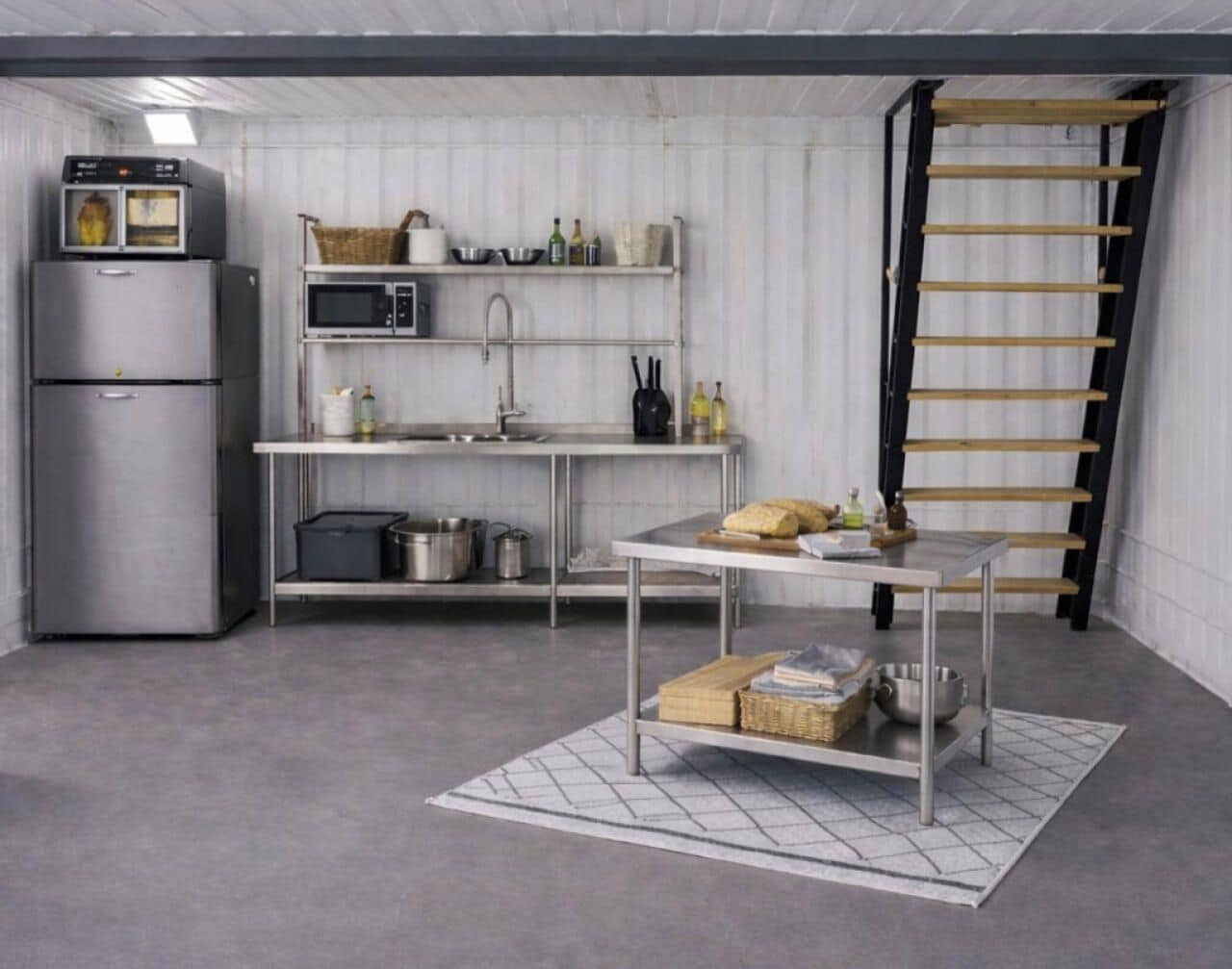 Une cuisine compacte dotée d’appareils électroménagers en acier inoxydable, d’une table en métal et d’une échelle appuyée contre le mur.