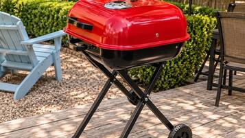 Een draagbare barbecue met wielen op een houten terras.