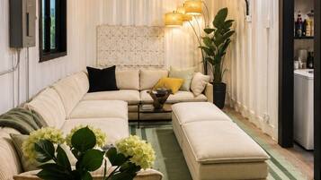 Een moderne woonkamer met een hoekbank, een salontafel met een bloevas, een vloerlamp en een groot raam.