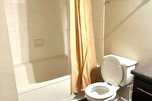 A bathroom with a white toilet, a shower area, and a beige tiled wall. - Modern Comfort Getaway- 2bd 1bath Free Parking (Woodland)