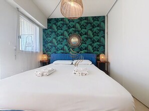 A hotel room with a large bed, two bedside tables with lamps, a wall with a leafy pattern, and a window with blinds. - Casa Port Latin: Terrace, Wi-Fi, beaches within walking distance (Fréjus)