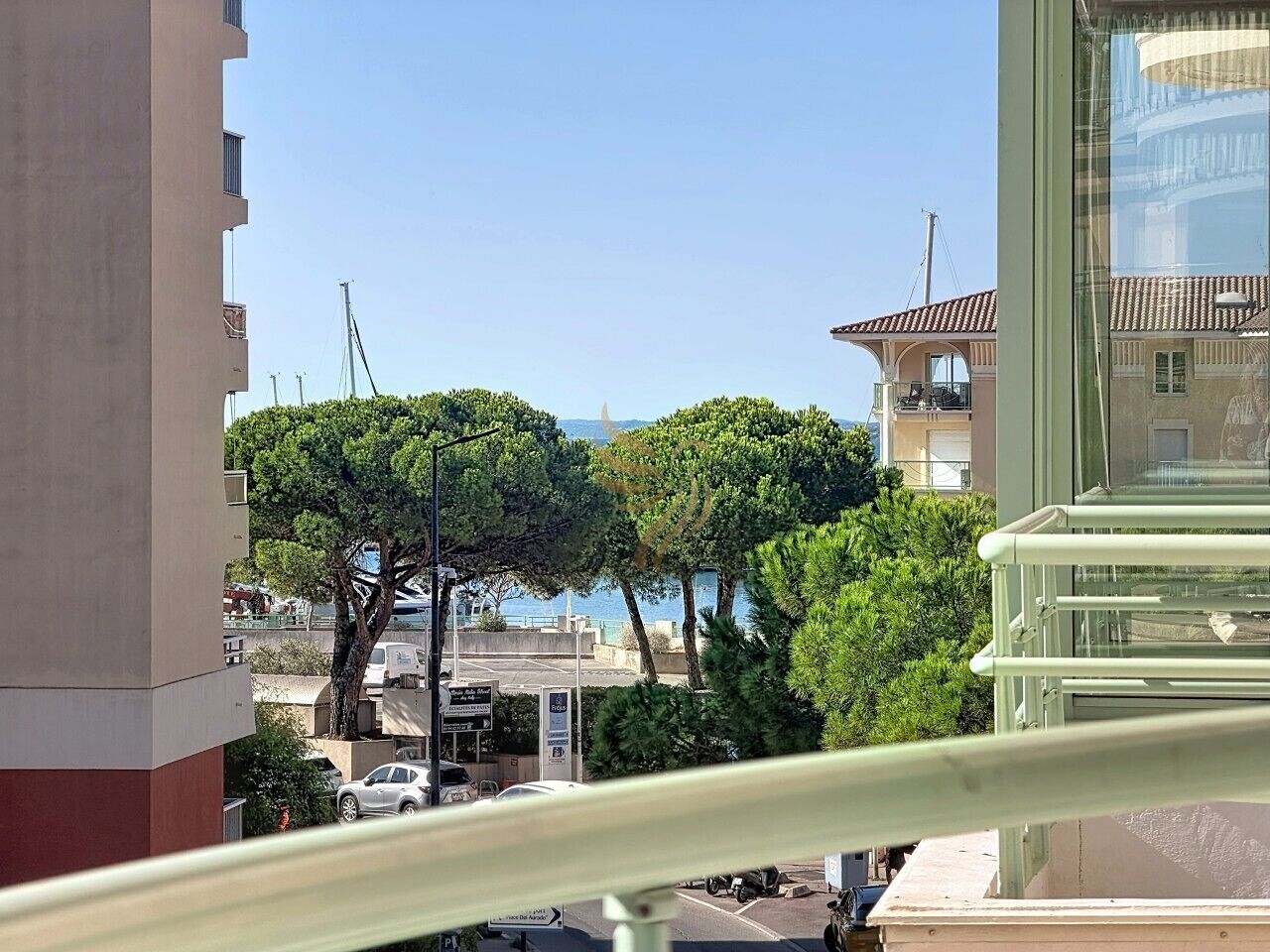 A balcony with a view of a coastal area, including trees and a building with a red roof.