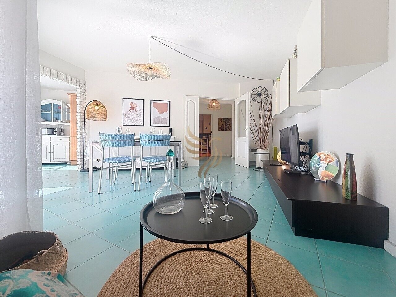 A modern living room with a dining area, a black coffee table with glasses, and a television on a black stand.