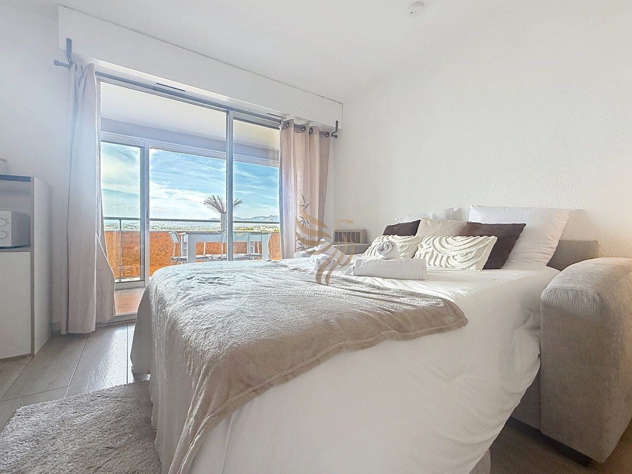 Une chambre à coucher avec un lit, une table de chevet, une fenêtre avec des rideaux et une vue sur l’extérieur.