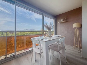 Ein modernes Zimmer mit einem großen Fenster, einem Esstisch mit Stühlen, einer Stehlampe und einem Regal mit Dekoration.