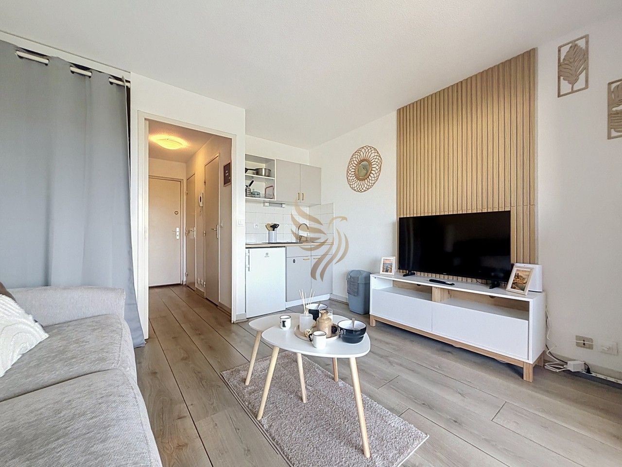 Un salon moderne avec un canapé, une table basse, un téléviseur et, au fond, un coin cuisine.
