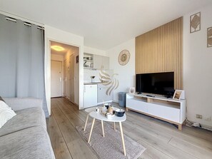 Ein modernes Wohnzimmer mit einer Couch, einem Couchtisch, einem Fernseher und einer Küche im Hintergrund.