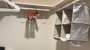 A baby crib with a quilted mattress, a hanging storage unit with fabric pockets, and a white wall with a light switch.