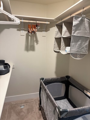 A baby crib with a quilted mattress, a hanging storage unit with fabric pockets, and a white wall with a light switch.