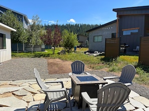 An outdoor patio with stone flooring, a table, and Adirondack chairs.