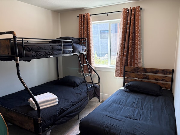 A dormitory room with bunk beds, a window with curtains, and a radiator.