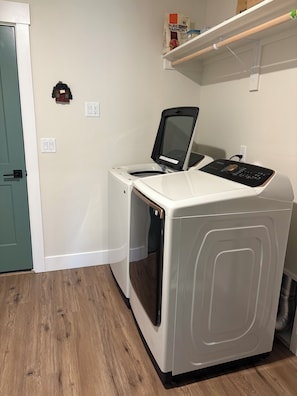 A compact, white washing machine with a control panel, situated in a room with wooden flooring and a green door.
