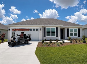 A residential building with a garage, a golf cart parked in front, and a well-maintained lawn. - New Designer Home · Complimentary Golf Cart · Prime Location in The Villages (Sumterville)