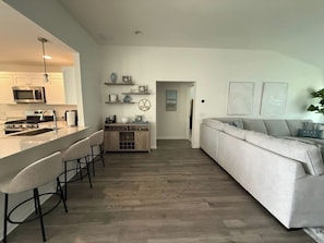 A modern kitchen with a bar area, a dining table, and a sofa in a living room. - New Designer Home · Complimentary Golf Cart · Prime Location in The Villages (Sumterville)