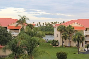 A hotel with multiple-story buildings, a well-maintained lawn, and a body of water in the background. - NSB Coastal Escape - 3BR Riverside Condo (New Smyrna Beach)