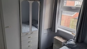 Une chambre avec une armoire, un lit, une fenêtre et une petite table de chevet.