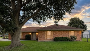A two-story brick house with a well-maintained lawn and a large tree in the foreground. - 3-bedroom, 2-bath home in Nederland with fence (nederland)