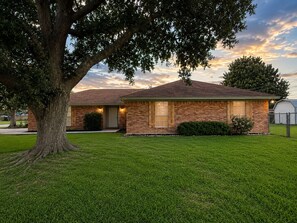 Une maison à deux étages, construite en briques, avec une pelouse bien entretenue et un grand arbre au premier plan.