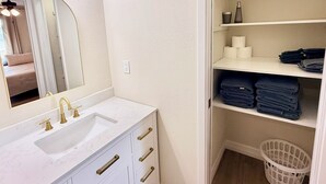 A bathroom with a white vanity, a large mirror, and a shelf with towels. - 3-bedroom, 2-bath home in Nederland with fence (nederland)