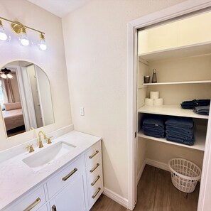 Une salle de bain avec un meuble-lavabo blanc, un grand miroir et une étagère avec des serviettes.