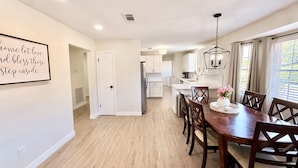A modern kitchen with white cabinets, a stainless steel refrigerator, and a dining area with a wooden table and chairs. - 3-bedroom, 2-bath home in Nederland with fence (nederland)