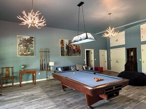 Et værelse med et poolbord, et billardstativ, en lampe og et billede på væggen.