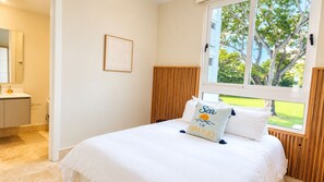 Ein Schlafzimmer mit einem Bett, einem Fenster mit Blick auf Grünflächen, einem Nachttisch und einem an der Wand hängenden Bild.
