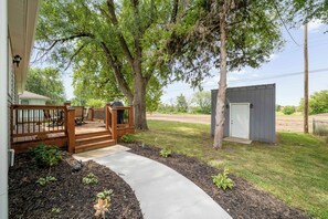 A residential property with a wooden deck, a small shed, and a pathway leading to a house.