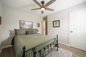 A bedroom with a bed, a ceiling fan, a door, and two framed pictures on the wall.
