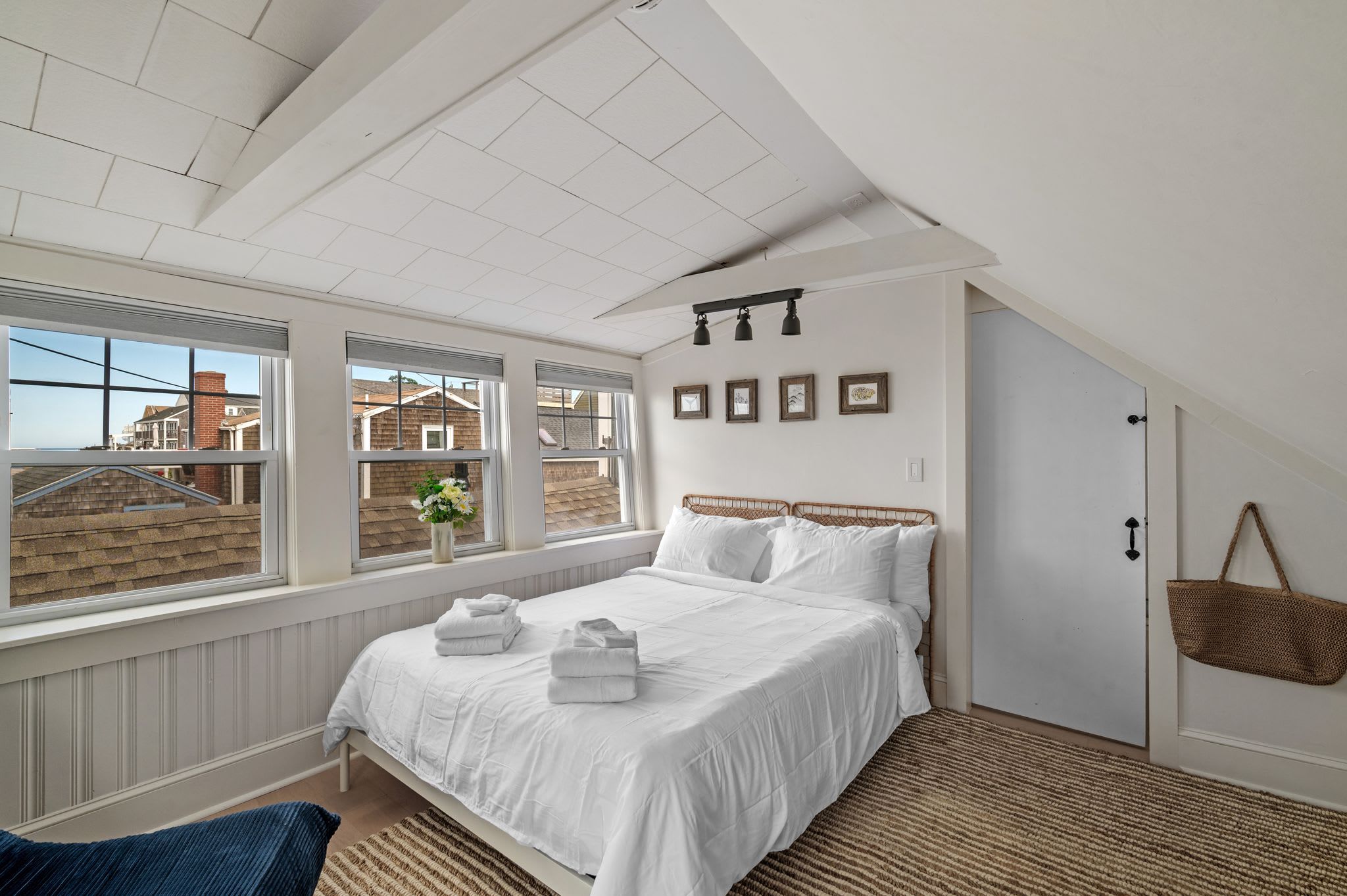 Een slaapkamer met een groot bed, een raam met uitzicht op huizen, en een deur met een mand eraan.