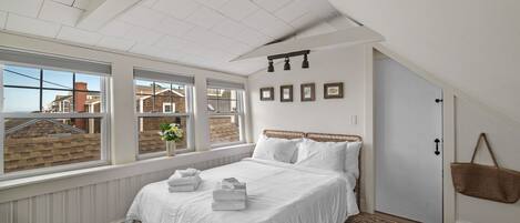 Een slaapkamer met een groot bed, een raam met uitzicht op huizen, en een deur met een mand eraan.