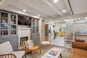 A modern living room with a fireplace, seating area, and a view into the kitchen.