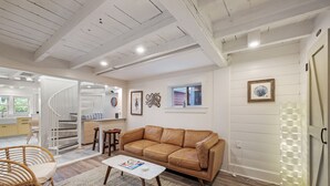 Ein geräumiger Wohnbereich mit einem braunen Ledersofa, einem weißen Couchtisch und einem Korbstuhl. Eine Treppe führt zu einer oberen Ebene, und ein Fenster sorgt für natürliches Licht.