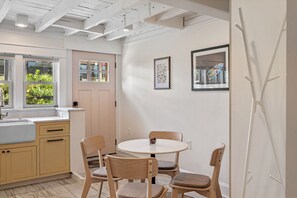 Une cuisine avec une table ronde, deux chaises, une fenêtre donnant sur un espace verdoyant et une porte avec un luminaire.