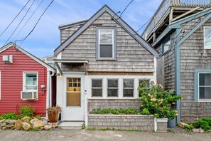 Une maison à deux étages avec un porche à l’avant, un bâtiment avec un revêtement rouge sur le côté gauche et un bâtiment avec un toit en bardeaux bleus sur le côté droit.