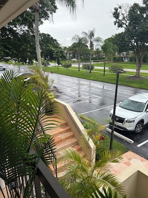 A residential street with a white car parked on the side, a staircase leading to a building, and lush greenery. - 2-bedroom apartment in peaceful Delray Beach with AC (Delray Beach)