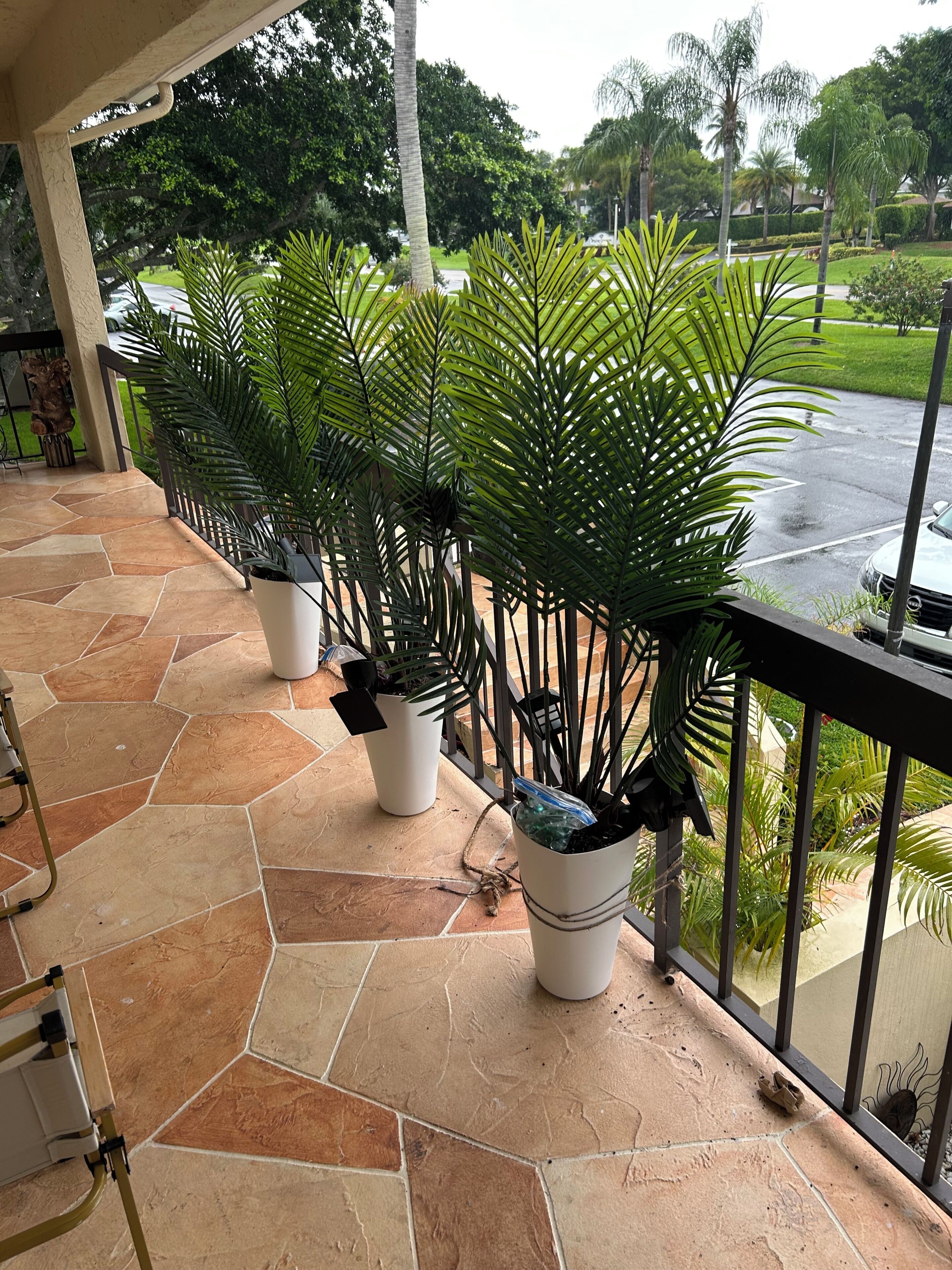 A covered outdoor area with potted plants, a stone floor, and a view of a road and greenery in the background.