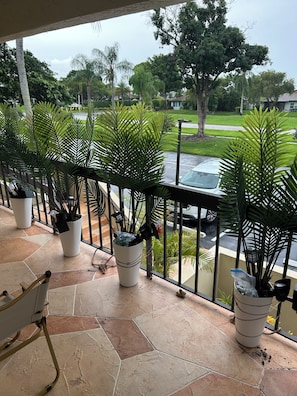 A balcony with potted plants, a chair, and a view of a street with cars and houses. - 2-bedroom apartment in peaceful Delray Beach with AC (Delray Beach)