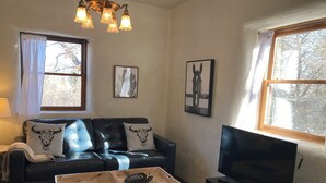 Ein Wohnzimmer mit einer Ledersofa, zwei Zierkissen, einem Holztisch, einem Fernseher und einer Kristallleuchter.