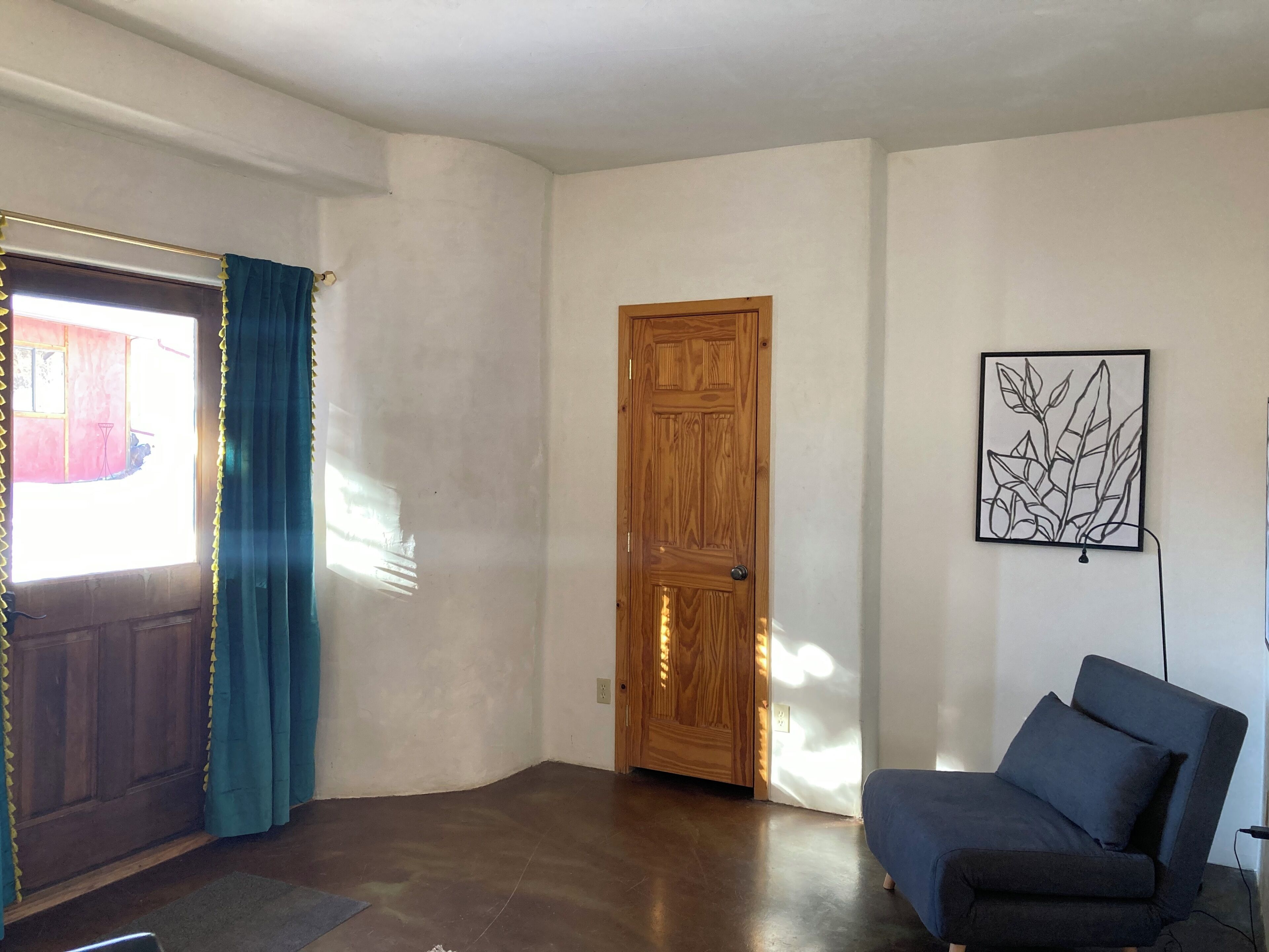 A room with a wooden door, a blue chair, and a framed artwork on the wall.