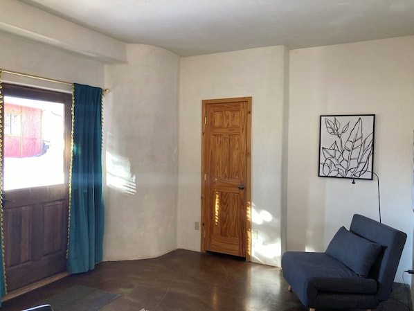 A room with a wooden door, a blue chair, and a framed artwork on the wall.