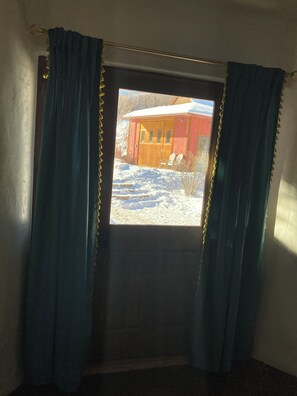 A room with a window, curtains, and a view of a red building outside.
