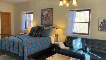 A bedroom with a bed, a nightstand, a lamp, a sofa, and a window.