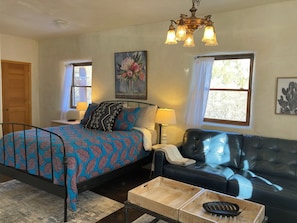 A bedroom with a bed, a nightstand, a lamp, a sofa, and a window.
