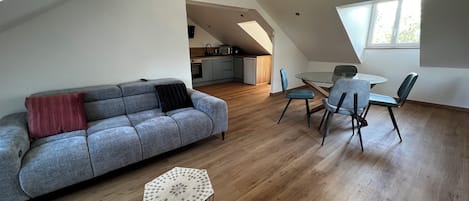 A modern living space with a grey sofa, a small octagonal table, and a dining area with chairs.