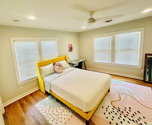 A bedroom with a bed, a desk, and two windows with blinds. - Chic Downtown Home (San Antonio)