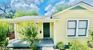 A single-story yellow house with a green door, a small porch, and a number '921' on the wall. - Chic Downtown Home (San Antonio)